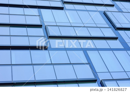 A tall building displays its glass facade with numerous reflective windows. The sunlight highlights the clean lines and symmetry of this urban architecture 141826827