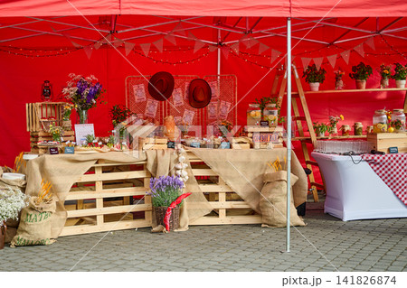 Warsaw, Poland, June 18, 2026 People gather around a market stall with a red tent, showcasing flowers and local food items in a lively outdoor space Warsaw, Poland, June 18, 2026 People gather around a market stall with a red tent, showcasing flowers and local food items in a lively outdoor space 141826874