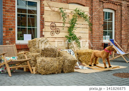 Warsaw, Poland, June 18, 2026 A market features hay bales stacked next to a wooden horse toy. Wooden chairs are set up nearby. The scene shows a brick building in the background Warsaw, Poland, June 18, 2026 A market features hay bales stacked next to a wooden horse toy. Wooden chairs are set up nearby. The scene shows a brick building in the background 141826875