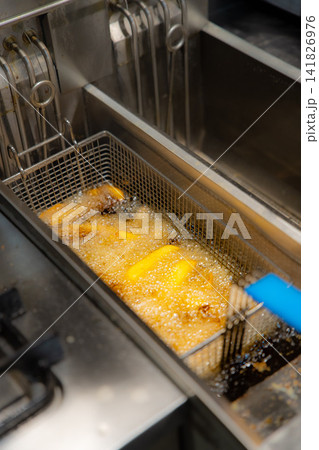 Basket of dices potatoes in the deep fryer of a restaurant kitchen. Overhead view Basket of dices potatoes in the deep fryer of a restaurant kitchen. Overhead view 141826976
