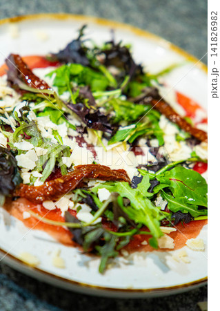 Beef Carpaccio cold appetizer with parmesan and arugula on a plate. Grey background. Top view. Beef Carpaccio cold appetizer with parmesan and arugula on a plate. Grey background. Top view. 141826982