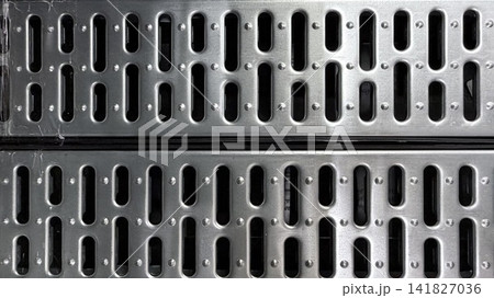 Close-up of perforated metal grate texture with repeating industrial pattern and dark openings. Close-up of perforated metal grate texture with repeating industrial pattern and dark openings. 141827036