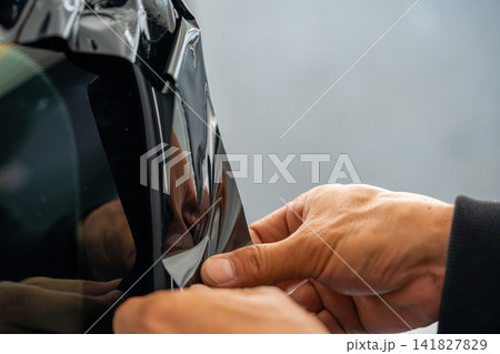 A car wrapping specialist applies a polyurethane film to the car. Detailer PPF A car wrapping specialist applies a polyurethane film to the car. Detailer PPF 141827829