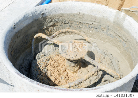 Cement mixer with gray mortar and tan sand churning inside. Blades partially visible, stirring materials to prepare construction-grade concrete mix Cement mixer with gray mortar and tan sand churning inside. Blades partially visible, stirring materials to prepare construction-grade concrete mix 141831307