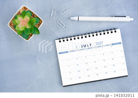 July 2027 desk calendar for 2026 and plant pot with pen on blue cement, Flat lay. 141832011