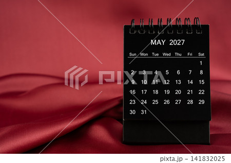 Black desk calendar for May 2027 on a red color satin or silk textile background. Black desk calendar for May 2027 on a red color satin or silk textile background. 141832025