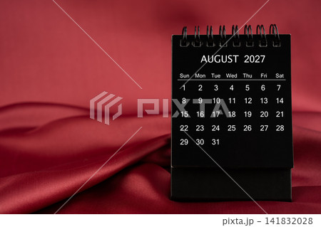 Black desk calendar for August 2027 on a red color satin or silk textile background. Black desk calendar for August 2027 on a red color satin or silk textile background. 141832028