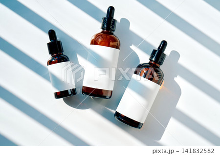 Cosmetic serum dropper bottles on white surface with shadows Cosmetic serum dropper bottles on white surface with shadows 141832582