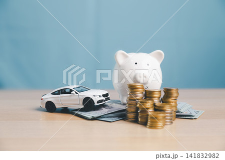 Piggy bank with white toy car, coin stacks, and cash, representing saving money for car purchase, down payment, auto loan planning, vehicle finance, and ownership budget. Piggy bank with white toy car, coin stacks, and cash, representing saving money for car purchase, down payment, auto loan planning, vehicle finance, and ownership budget. 141832982