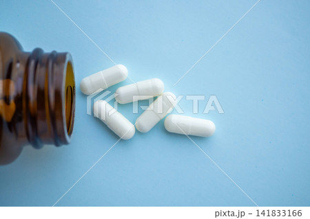 medicine pills capsule spilling out of bottle on blue background medicine pills capsule spilling out of bottle on blue background 141833166