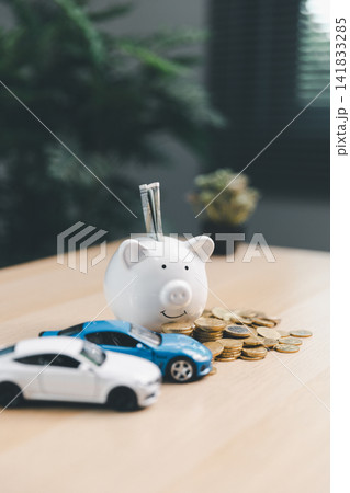 Piggy bank with cash, coins, and miniature cars on a desk, illustrating car savings, auto loan planning, vehicle insurance, personal finance, and transportation budget concept. Piggy bank with cash, coins, and miniature cars on a desk, illustrating car savings, auto loan planning, vehicle insurance, personal finance, and transportation budget concept. 141833285