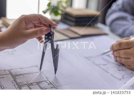 Architect using compass to draw and measure drawing on blueprint in office. 141833753