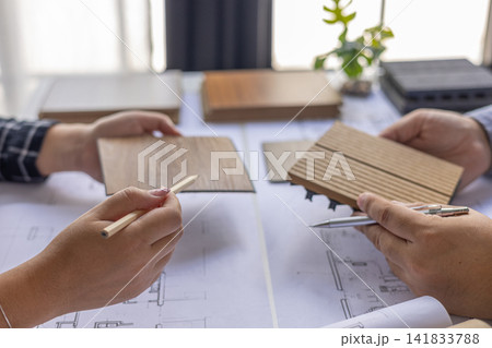 Architects and designers collaborating on a project by examining blueprints and material samples. Architects and designers collaborating on a project by examining blueprints and material samples. 141833788