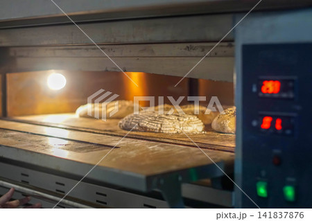 Fresh artisan bread loaves baking inside a professional bakery oven. Warm lighting and rustic dough texture show traditional baking process. 141837876