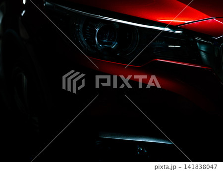 Closeup headlight of shiny red luxury SUV compact car. Elegant electric car technology and business concept. Hybrid auto and automotive concept. Car parked in showroom or motor show. Car dealership. 141838047