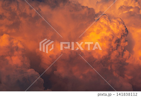 Orange cumulonimbus storm clouds illuminated by golden sunset light. Cloudscape with dense textures, glowing formations and powerful weather background. Weather, climate and abstract sky background. Orange cumulonimbus storm clouds illuminated by golden sunset light. Cloudscape with dense textures, glowing formations and powerful weather background. Weather, climate and abstract sky background. 141838112