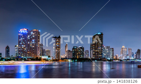 Panoramic Bangkok cityscape at night featuring illuminated skyscrapers beside Chao Phraya River. Urban architecture in Thailand modern capital. Modern waterfront architecture. Metropolitan landscape. Panoramic Bangkok cityscape at night featuring illuminated skyscrapers beside Chao Phraya River. Urban architecture in Thailand modern capital. Modern waterfront architecture. Metropolitan landscape. 141838126