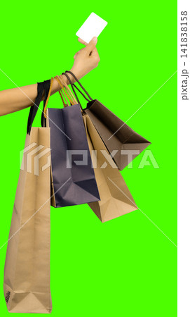 Woman holding shopping bags and a blank credit card isolated on a green chroma key background for Black Friday sales, consumer spending, cashless payment, retail marketing, and ecommerce promotion. Woman holding shopping bags and a blank credit card isolated on a green chroma key background for Black Friday sales, consumer spending, cashless payment, retail marketing, and ecommerce promotion. 141838158