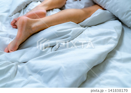 Woman barefoot on bed over white linen blanket and bed sheet in hotel or home bedroom. Sleep and relaxation. Lazy Sunday morning. Bare feet of woman chilling sleep on white comfort bed and duvet. Woman barefoot on bed over white linen blanket and bed sheet in hotel or home bedroom. Sleep and relaxation. Lazy Sunday morning. Bare feet of woman chilling sleep on white comfort bed and duvet. 141838170