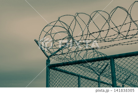 Prison security fence. Barbed wire security fence. Razor wire jail fence. Barrier border. Boundary security wall. Prison for arrest criminals or terrorists. Private area. Military zone concept. Prison security fence. Barbed wire security fence. Razor wire jail fence. Barrier border. Boundary security wall. Prison for arrest criminals or terrorists. Private area. Military zone concept. 141838305