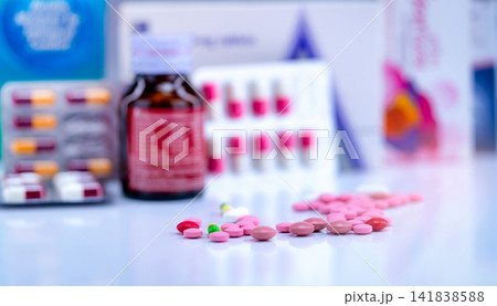 Tablets and capsule pills on blurred drug bottle, capsule in blister pack and paper box package of medicine. Pink and red tablets and green-yellow capsule on pharmacy counter. Pharmaceutical industry. Tablets and capsule pills on blurred drug bottle, capsule in blister pack and paper box package of medicine. Pink and red tablets and green-yellow capsule on pharmacy counter. Pharmaceutical industry. 141838588