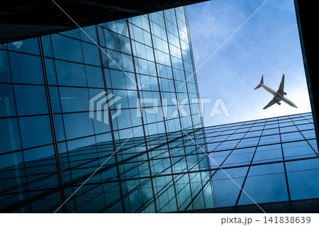 Airplane flying above modern glass office building. Perspective view of futuristic glass building. Exterior of office glass building. Business trip. Reflection in transparent glass. Company window. Airplane flying above modern glass office building. Perspective view of futuristic glass building. Exterior of office glass building. Business trip. Reflection in transparent glass. Company window. 141838639