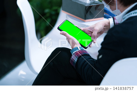 Person holding modern smartphone with green screen mockup while sitting indoors, perfect for mobile application, website presentation, user interface, digital marketing and technology concepts. 141838757