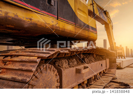 Closeup dirt track pad of backhoe. Digger parked at construction site. Bulldozer near concrete pole. Earth moving machine. Yellow digger with bucket. Earth moving machine. Excavation vehicle. 141838848