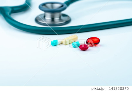 Stethoscope with blue-white capsule, red soft gel capsule pills, and red round tablets on doctor table or nurse desk. Medical healthcare and medicine background. Cardiology doctor diagnosis equipment. 141838870