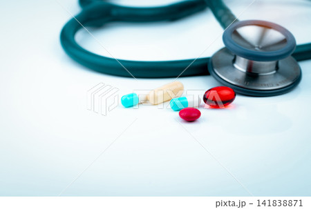 Stethoscope with blue-white capsule, red soft gel capsule pills, and red round tablets on doctor table or nurse desk. Medical healthcare and medicine background. Cardiology doctor diagnosis equipment. Stethoscope with blue-white capsule, red soft gel capsule pills, and red round tablets on doctor table or nurse desk. Medical healthcare and medicine background. Cardiology doctor diagnosis equipment. 141838871