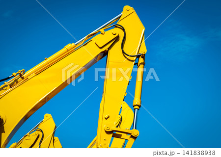 Yellow backhoe with hydraulic piston arm against clear blue sky. Heavy machine for excavation in construction site. Hydraulic machinery. Huge bulldozer. Heavy industry 141838938