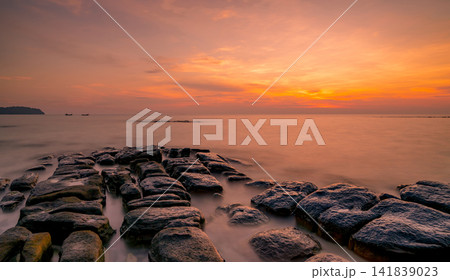 Long exposure sunset seascape with rugged coastal rocks, silky ocean water and glowing orange twilight sky, creating a peaceful tropical shoreline landscape. Tranquil coastal nature landscape. 141839023