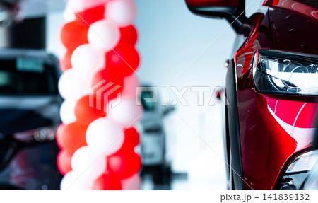 Modern red SUV displayed in car showroom with illuminated LED headlight and promotional balloons, premium automobile dealership interior for vehicle sales, automotive marketing and transportation. 141839132