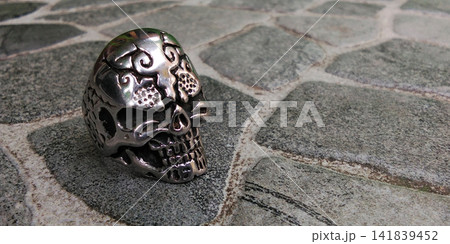 Silver skull ring with intricate details on gray stone tile background. Silver skull ring with intricate details on gray stone tile background. 141839452