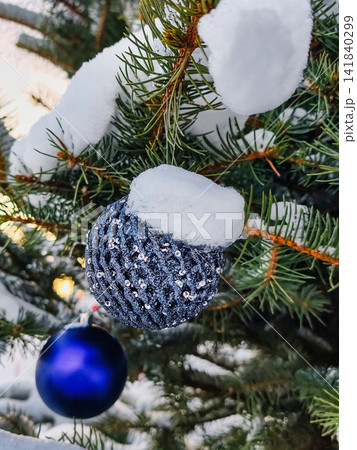 A natural Christmas tree stands in a snowy area. The tree is decorated with shiny ornaments and a layer of snow covers the branches during winter celebrations A natural Christmas tree stands in a snowy area. The tree is decorated with shiny ornaments and a layer of snow covers the branches during winter celebrations 141840299