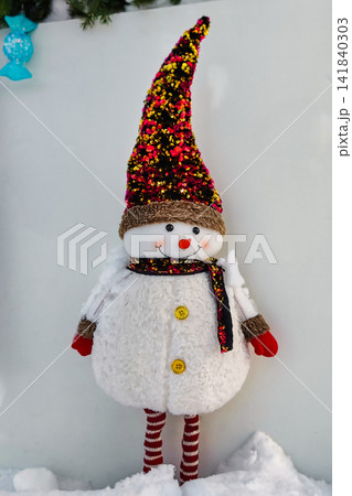 A natural Christmas tree stands tall with bright decorations. Nearby, a snowman figure in winter clothing adds joy to the festive event during New Year celebrations A natural Christmas tree stands tall with bright decorations. Nearby, a snowman figure in winter clothing adds joy to the festive event during New Year celebrations 141840303