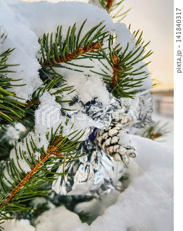 A Christmas tree is decorated with ornaments and snow. It stands outdoors in winter showing nature and holiday spirit during the New Year period A Christmas tree is decorated with ornaments and snow. It stands outdoors in winter showing nature and holiday spirit during the New Year period 141840317