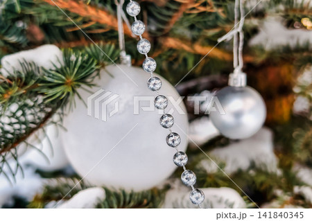 The Christmas tree stands decorated with shiny ornaments and garland. Snow sits on the branches as people celebrate New Year and Christmas with joy The Christmas tree stands decorated with shiny ornaments and garland. Snow sits on the branches as people celebrate New Year and Christmas with joy 141840345