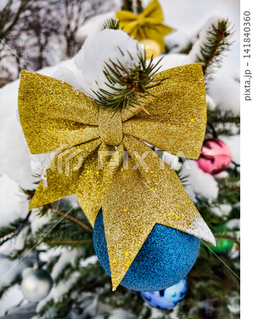 A Christmas tree stands covered in snow with colorful ornaments and a golden bow. This scene captures the holiday spirit during winter festivities A Christmas tree stands covered in snow with colorful ornaments and a golden bow. This scene captures the holiday spirit during winter festivities 141840360