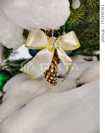 A natural Christmas tree stands with decorations and gifts under snow. Pine cones hang from branches, showing holiday spirit. Children play nearby A natural Christmas tree stands with decorations and gifts under snow. Pine cones hang from branches, showing holiday spirit. Children play nearby 141840361