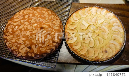 Homemade apple tart topped with sliced apples alongside an almond topped pastry cooling on a wire rack after baking. Homemade apple tart topped with sliced apples alongside an almond topped pastry cooling on a wire rack after baking. 141840771