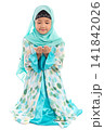 Charming young Asian Muslim child in traditional headscarf kneeling politely holding hands up in prayer looking down. 141842026
