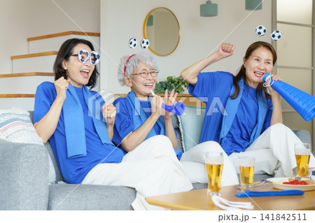 リビングのソファに並んで座ってテレビでサッカー日本代表を応援するミドル世代の日本人女性3人 リビングのソファに並んで座ってテレビでサッカー日本代表を応援するミドル世代の日本人女性3人 141842511