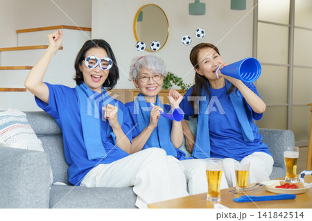 リビングのソファに並んで座ってテレビでサッカー日本代表を応援するミドル世代の日本人女性3人 リビングのソファに並んで座ってテレビでサッカー日本代表を応援するミドル世代の日本人女性3人 141842514