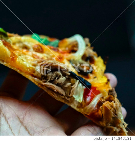 Close-up of a cheesy pizza slice with tuna, onion and olives held in a hand. Fast food, takeaway pizza and casual eating lifestyle concept. Close-up of a cheesy pizza slice with tuna, onion and olives held in a hand. Fast food, takeaway pizza and casual eating lifestyle concept. 141843151