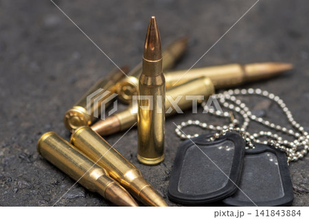 Rifle cartridges standing among scattered ammunition and military dog tags Rifle cartridges standing among scattered ammunition and military dog tags 141843884