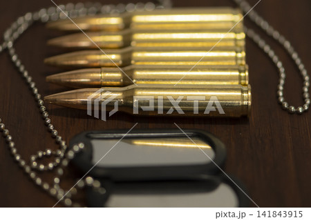 Closeup of rifle cartridges and dog tags arranged on wooden surface 141843915