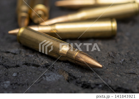 Close up of rifle cartridges lying on rough dark asphalt surface Close up of rifle cartridges lying on rough dark asphalt surface 141843921