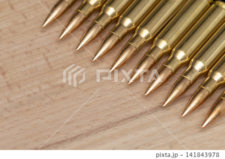 Closeup of rifle cartridges aligned diagonally on a light wooden surface 141843978