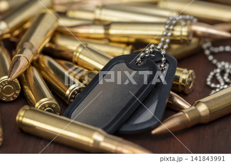 Military dog tags lying on rifle cartridges in closeup still life 141843991